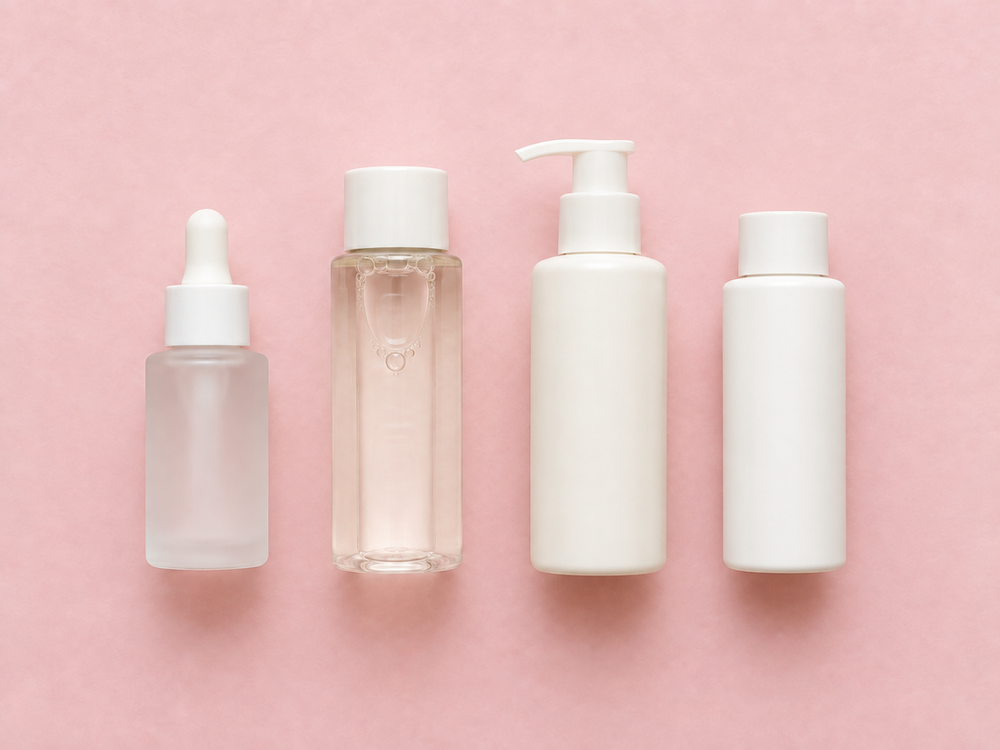 Four skincare bottles lined up in order on a pink background